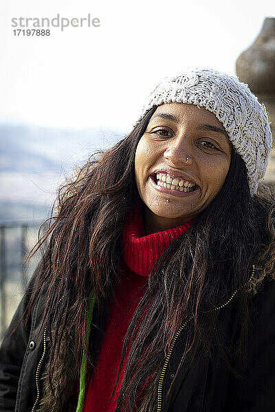 Eine schöne junge Frau lächelnd mit Piercings im Park mit Wintermütze