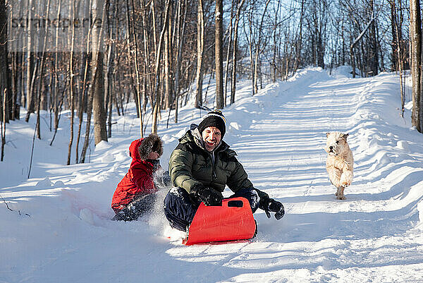 Vater und Sohn rodeln an einem Wintertag mit ihrem Hund einen verschneiten Hügel hinunter.
