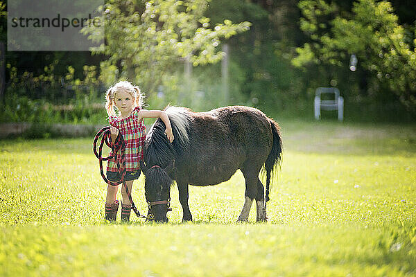 Niedliches kleines blondes Mädchen mit Arm um schwarzes Pony.