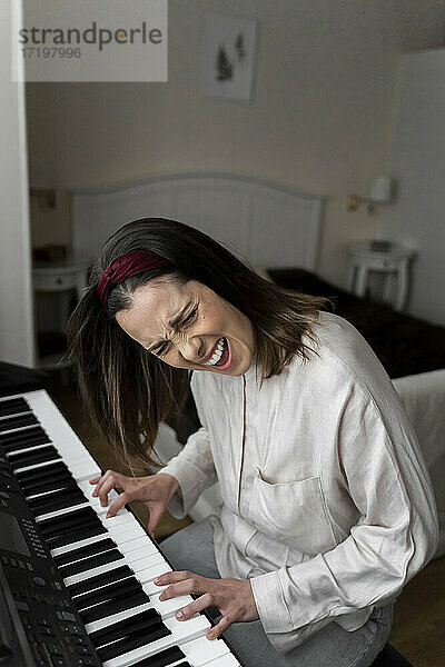 Fröhliche junge Frau singt beim Klavierspielen im Schlafzimmer