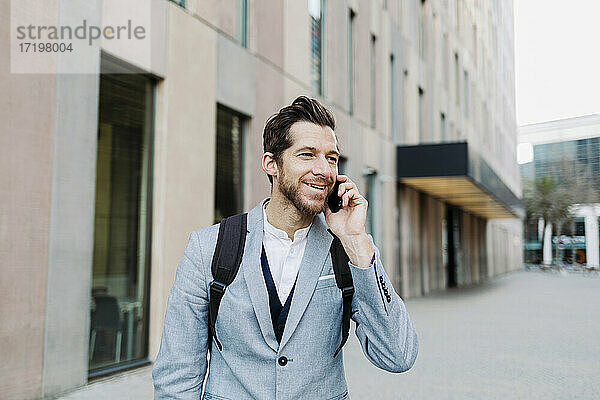 Lächelnder männlicher Berufstätiger  der mit dem Handy telefoniert und dabei wegschaut