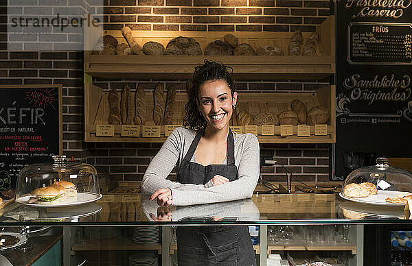 Lächelnde Frau steht vor einem Regal mit Backwaren in einer beleuchteten Bäckerei