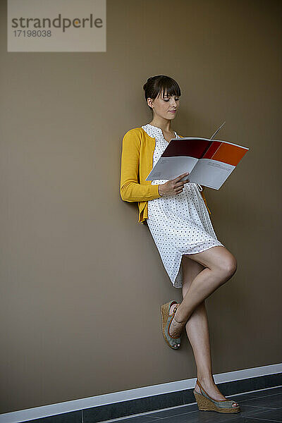 Weibliche Geschäftsfrau liest Dokumente und lehnt sich an die Wand