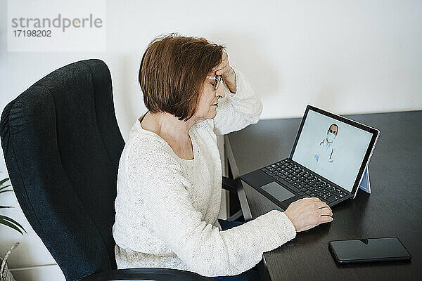 Frau  die unter Kopfschmerzen leidet  lässt sich von einem Arzt per Videoanruf über ihren Laptop zu Hause beraten