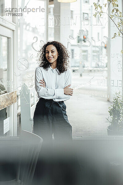 Lächelnde Geschäftsfrau steht mit verschränkten Armen im Café