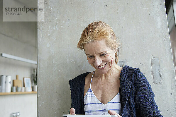 Lachende Frau  die ein digitales Tablet gegen eine Säule zu Hause benutzt