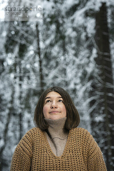 Junge Frau mit Pullover  die im Wald steht und nach oben schaut