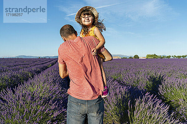 Vater trägt seine kleine Tochter in einem großen Lavendelfeld im Sommer