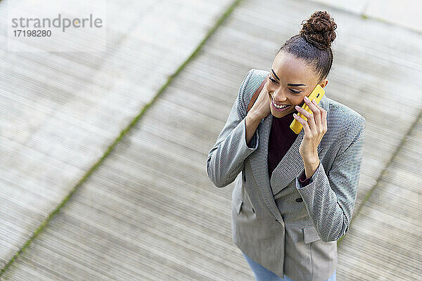 Lächelnde Geschäftsfrau  die auf dem Gehweg stehend mit ihrem Handy telefoniert