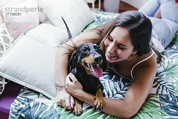 Lächelnde Frau  die ihren Hund umarmt  während sie zu Hause auf dem Bett liegt