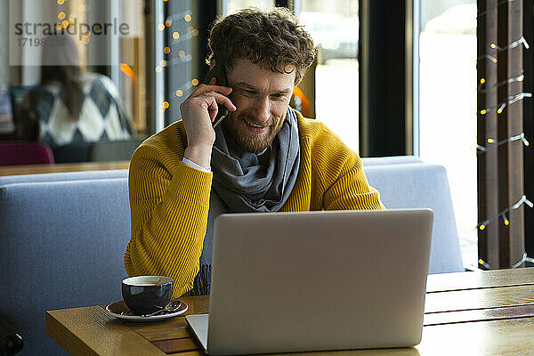 Gut aussehender Geschäftsmann  der in einem Café mit seinem Laptop telefoniert