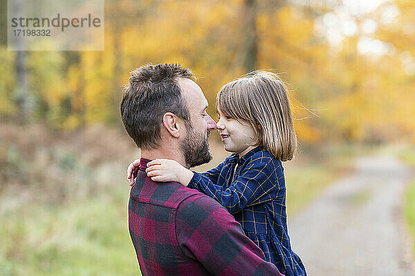 Lächelnder Vater und Tochter reiben sich die Nase  während sie im Wald stehen