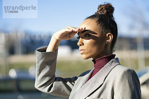 Junge Geschäftsfrau  die ihre Augen schützt  während sie an einem sonnigen Tag im Freien steht