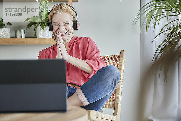 Lächelnde Frau grüßt während eines Videoanrufs auf dem Laptop zu Hause