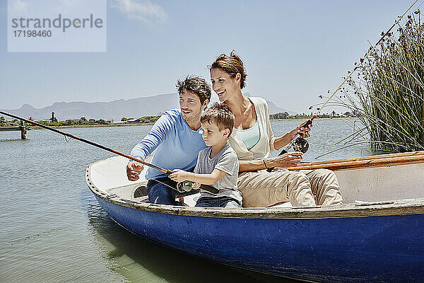 Eltern mit Angelrute sitzen neben dem Sohn im Ruderboot auf dem See