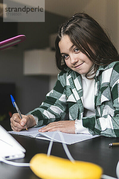 Lächelndes Mädchen studiert am Tisch im Wohnzimmer