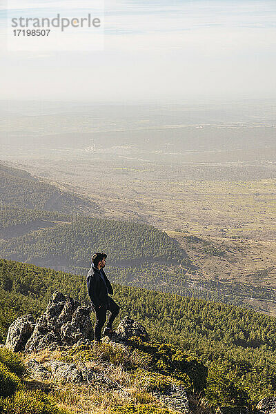 Männlicher Wanderer  der die Aussicht betrachtet  während er auf einem Felsen in Somosierra  Madrid  Spanien steht