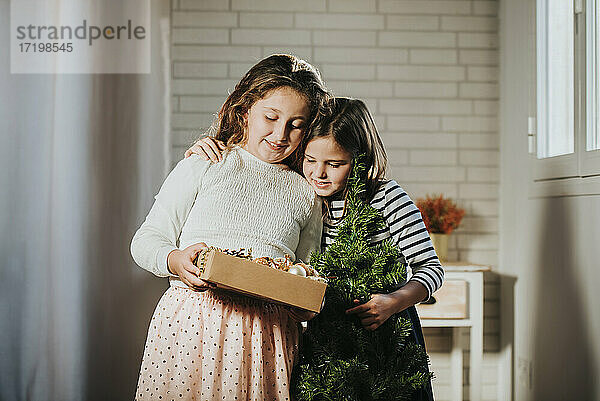 Mädchen mit Kiefer Weihnachten umarmt Schwester hält Weihnachtsschmuck Box zu Hause