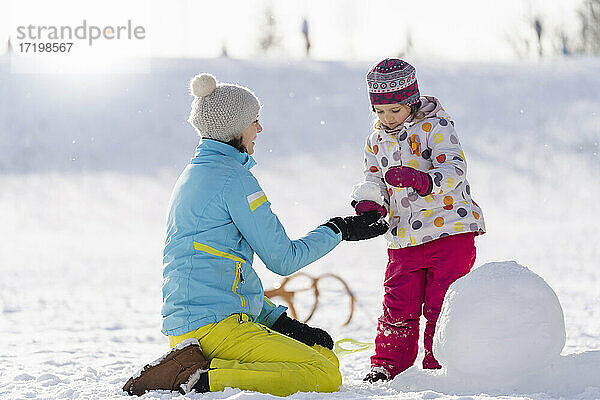Mutter hilft Tochter beim Schneemannbau im Park