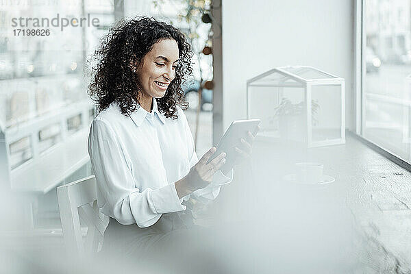 Junge Geschäftsfrau lächelt  während sie in einem Café sitzt und ein digitales Tablet benutzt