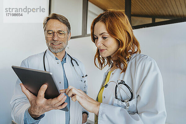 Allgemeinmediziner bei der Arbeit an einem digitalen Tablet  während er neben einem Kollegen in der Klinik steht