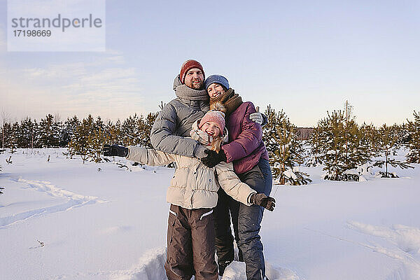 Glückliche Familie in warmer Kleidung auf Schnee stehend gegen den Himmel im Winter