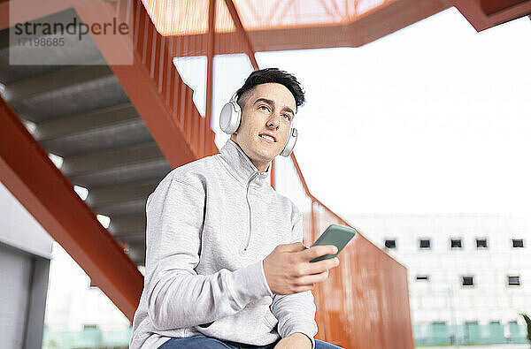 Junger Mann hört Musik  während er sein Smartphone an der Treppe benutzt
