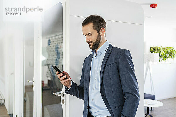Geschäftsmann  der ein Smartphone benutzt  während er an einer Telefonzelle im Büro steht