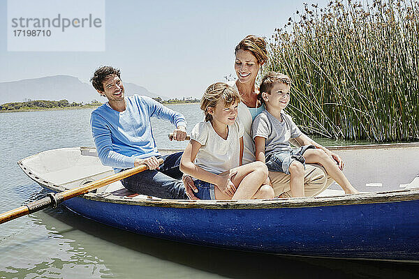 Älterer Mann paddelt  während er mit seiner Familie in einem Ruderboot an einem sonnigen Tag sitzt