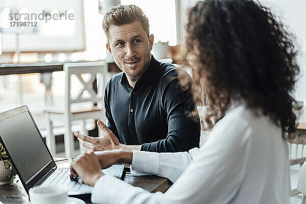 Geschäftsmann im Gespräch mit einem Kollegen  der einen Laptop benutzt  während er in einem Cafe sitzt