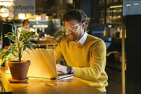 Lächelnder männlicher Besitzer arbeitet am Laptop  während er im Café sitzt