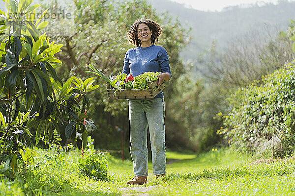 Lächelnde Frau mit Gemüsekiste im Garten stehend