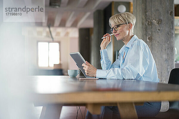 Lächelnde Geschäftsfrau  die ein digitales Tablet benutzt  während sie am Schreibtisch im Heimbüro sitzt