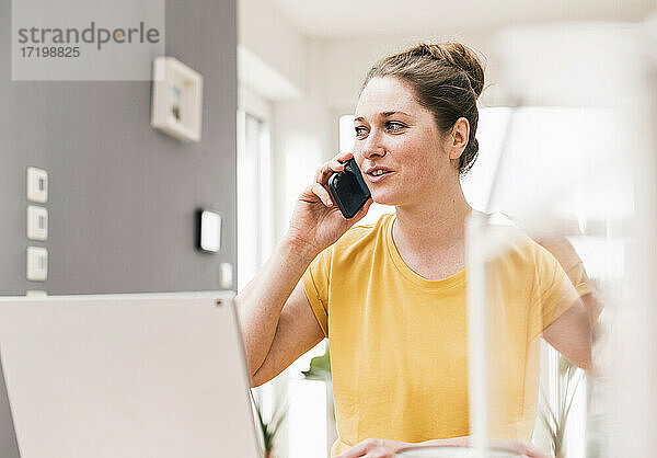 Unternehmerin  die bei der Arbeit zu Hause mit ihrem Smartphone telefoniert