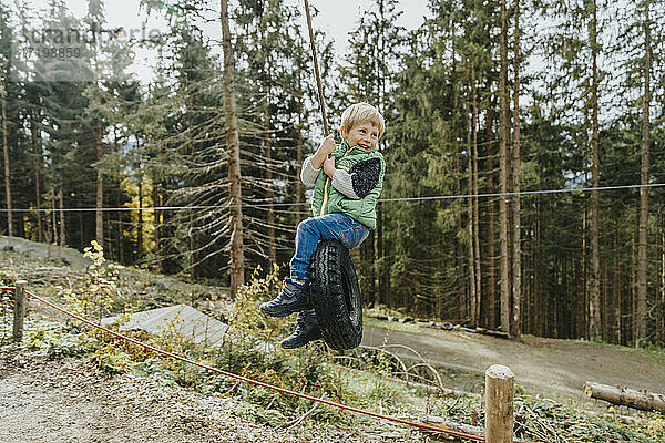 Junge sitzt auf einer Reifenschaukel im Wald während der Ferien im Salzburger Land  Österreich