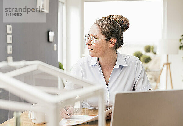 Geschäftsfrau mit Brille sitzt am Schreibtisch und schaut weg