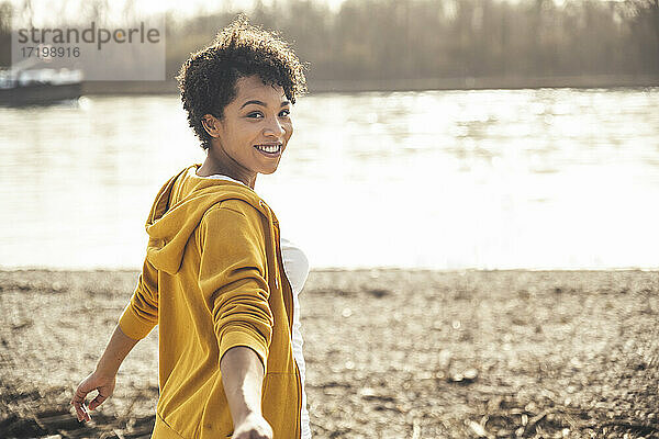 Junge Frau lächelt  während sie an einem sonnigen Tag am See steht