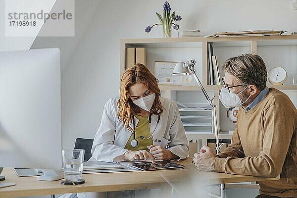 Arzt und Patient benutzen ein digitales Tablet  während sie in der Arztpraxis sitzen