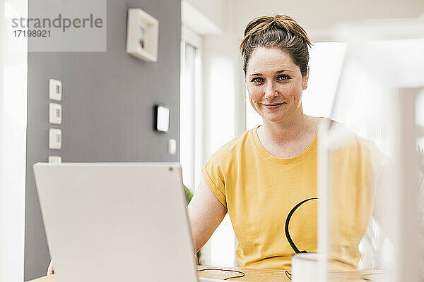 Lächelnde Geschäftsfrau sitzt mit Laptop zu Hause