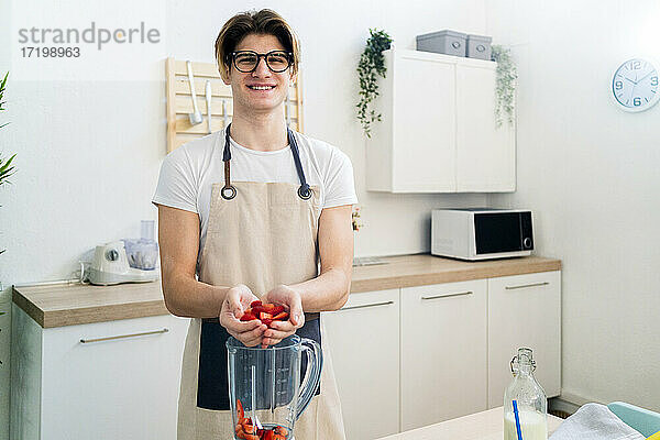 Lächelnder junger Mann gibt gehackte Erdbeeren in den Mixer