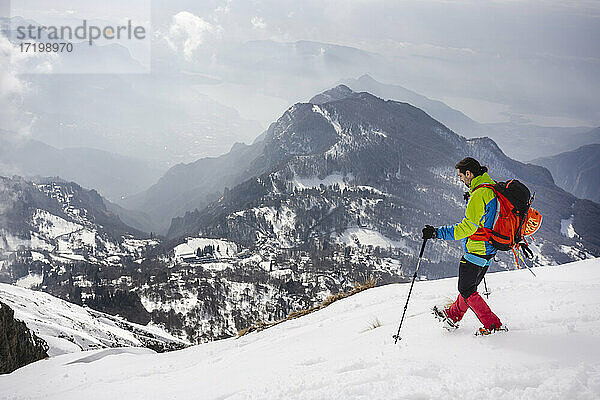 Männlicher Wanderer mit Rucksack und Wanderstock auf einem schneebedeckten Berg  der Steigeisen trägt