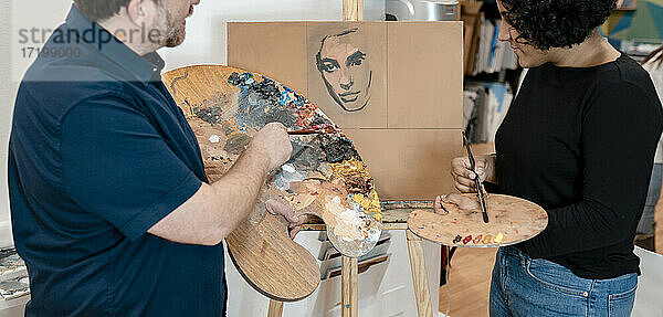 Junge Malerin lernt von einem männlichen Künstler im Atelier