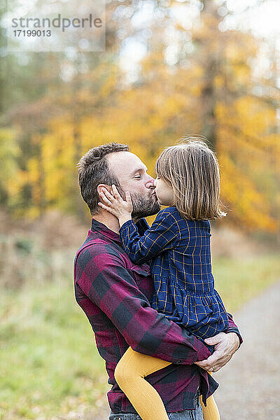 Vater küsst Tochter im Wald stehend