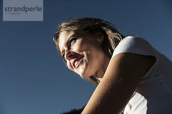 Lächelnde Frau schaut beim Sonnenbad gegen den Himmel weg