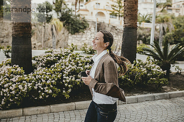 Fröhliche Frau mit Smartphone  die auf dem Fußweg läuft