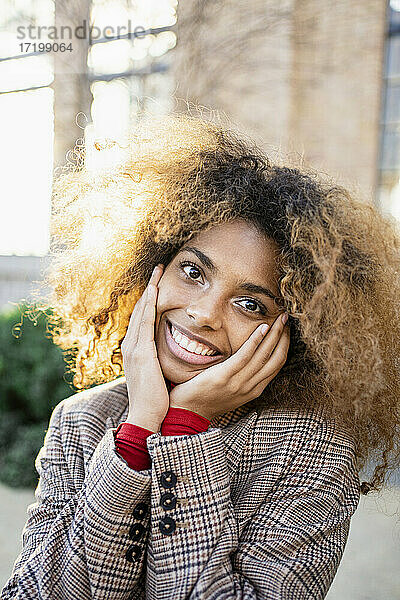Lächelnde Afro-Frau mit Kopf in den Händen vor einem Gebäude