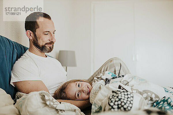 Lächelnde Tochter auf dem Schoß des Vaters auf dem Bett zu Hause liegend