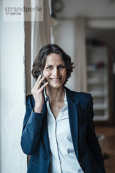 Lächelnde Geschäftsfrau  die zu Hause mit ihrem Smartphone telefoniert