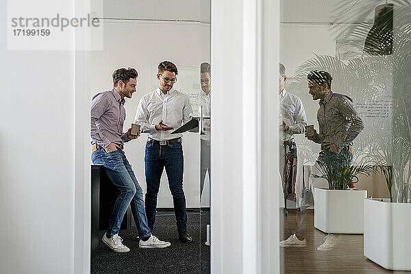 Männliche Unternehmer  die über ein Klemmbrett diskutieren  gesehen durch eine Tür im Büro