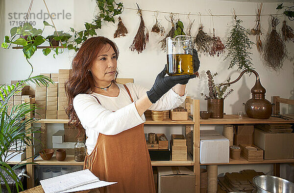 Frau hält Becher mit Olivenöl bei der Herstellung von Seife in einer Werkstatt